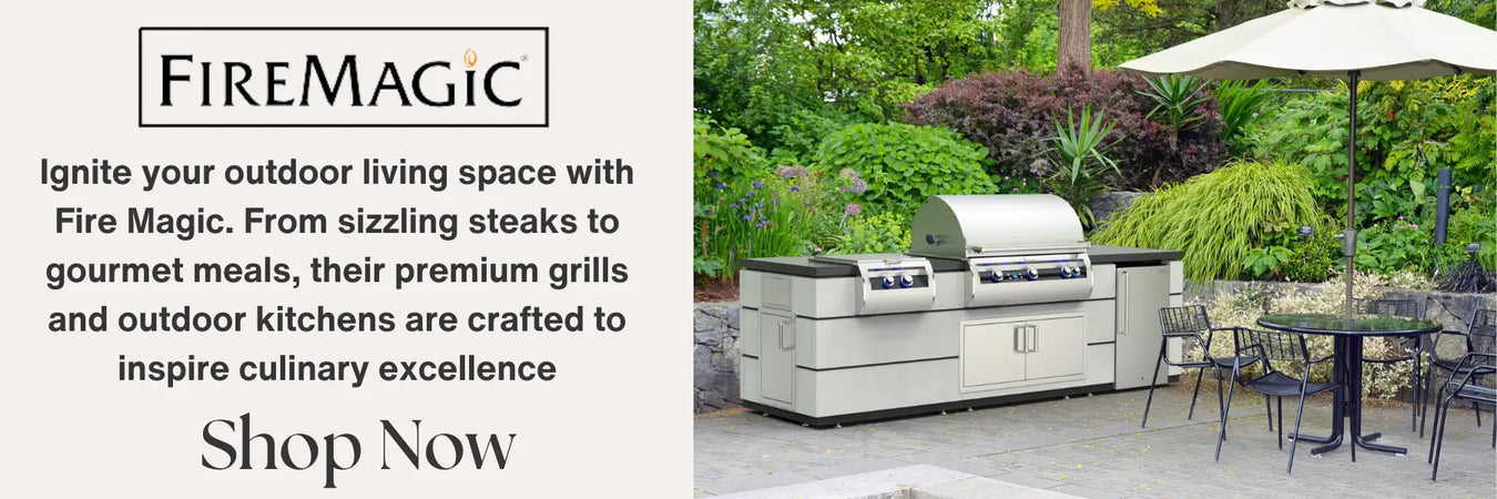 A stainless steel outdoor kitchen with a grill, side burner, and storage cabinets. The kitchen is set on a patio with a small table and chairs, surrounded by lush greenery. An umbrella provides shade above the table.