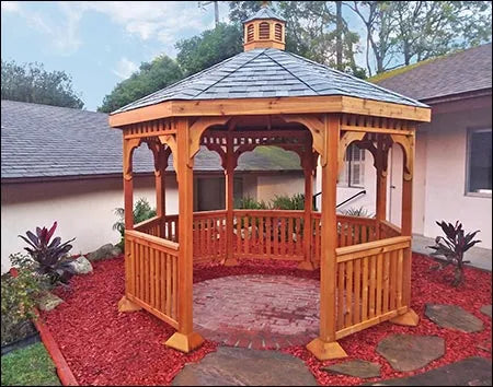 A wooden octagonal gazebo with a shingled roof and a decorative cupola. The gazebo features lattice detailing on the walls and a spacious interior with a brick floor.