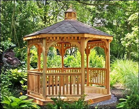 A wooden octagonal gazebo with a shingled roof and a decorative cupola. The gazebo features latticework detailing on the walls, a spacious interior with a brick floor, and a wooden bench.