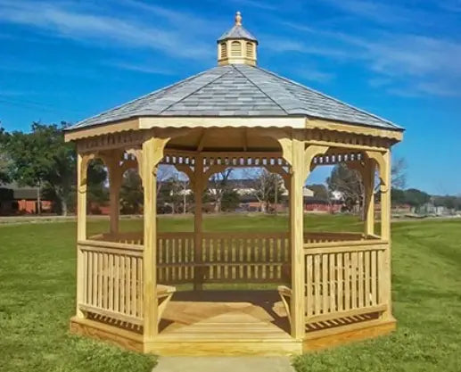 A large octagonal gazebo with a classic design. It features a shingled roof, decorative railings, and built-in benches. The gazebo is made of pressure-treated pine and is available in a variety of sizes.