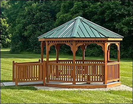 A wooden octagonal gazebo with a green metal roof. The gazebo has a decorative railing and is surrounded by a grassy area.