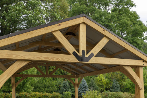  A person relaxing on a lounge chair under a wooden pavilion with a bronze-colored steel roof. The pavilion is surrounded by greenery