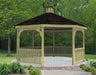 A large octagonal gazebo with a classic design. It features a shingled roof with a decorative cupola, and intricate latticework railings surrounding the open structure. The gazebo is painted a light tan color and sits on a concrete pad surrounded by greenery.