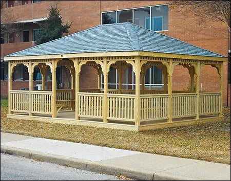 20 x 40 fifthroom wooden gazebo with a peaked roof and decorative latticework. The gazebo stands on a concrete base surrounded by greenery.