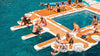 People enjoying a floating platform in the water with lounge chairs and a pool.