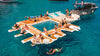 People enjoying a large inflatable pool party raft in the middle of a body of water with a boat nearby.