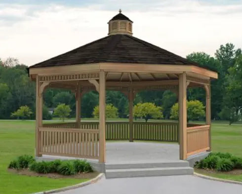 A large, octagonal wooden gazebo with a shingled roof, decorative cupola, and lattice detailing on the walls. The gazebo features a spacious interior with open latticework walls and is surrounded by a paved walkway and lush greenery.