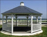 A white hexagonal gazebo with a gray shingled roof stands on a raised platform. The gazebo features decorative white railings and offers a view of a body of water.