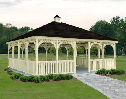 16 x 16 fifthroom wooden gazebo with a peaked roof and decorative latticework. The gazebo stands on a concrete base surrounded by greenery.