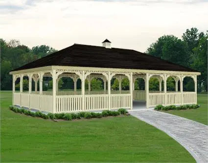 20 x 20 wooden gazebo with a peaked roof and decorative latticework. The gazebo stands on a concrete base surrounded by greenery.