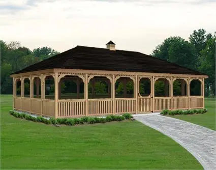 A large rectangular wooden gazebo with a peaked roof and screened walls. The gazebo features decorative latticework and multiple double doors with small windows. It is surrounded by a paved walkway and a lawn with mature trees in the background