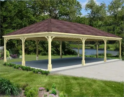 extra large pine wood gazebo with a gabled roof and a concrete base. The gazebo is surrounded by lush greenery and a lake is visible in the background.