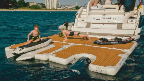 Two people on inflatable platform in the water with a boat in the background.