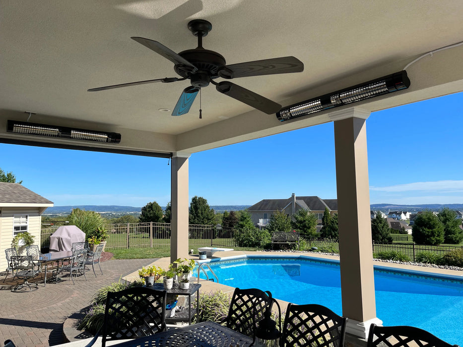 A spacious covered patio overlooking a pool and a scenic view. The patio features a ceiling fan, comfortable seating, and two electric heaters mounted on the ceiling to provide warmth and comfort on cooler evenings.