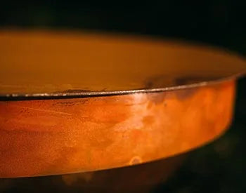 A close-up of the edge of a round, orange fire pit lid. The lid appears to be made of metal with a textured surface.