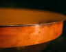 A close-up of the edge of a round, orange fire pit lid. The lid appears to be made of metal with a textured surface.