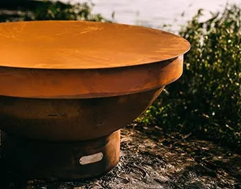 A round, orange fire pit with a matching orange lid. The lid is slightly raised, revealing the black interior of the fire pit.