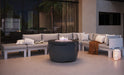 Contemporary outdoor patio with a round gray fire pit (Ledge Lounger Halo) as the central element, surrounded by a gray sectional sofa and warm string lights at dusk.