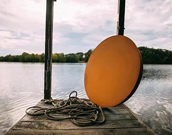 A round, orange fire pit lid leaning against a wooden post on a dock.