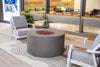 Real Flame Aegean Round Propane Fire Table in gray with lava rocks, surrounded by gray armchairs and a built-in seating area in a contemporary indoor space.