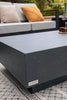 A close-up, low-angle shot focuses on a modern, dark gray rectangular coffee table with a textured surface, possibly concrete or a similar material.