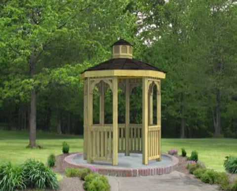 A large octagonal gazebo with a classic design. It features a shingled roof, decorative railings, and built-in benches. The gazebo is made of pressure-treated pine and is available in a variety of sizes.