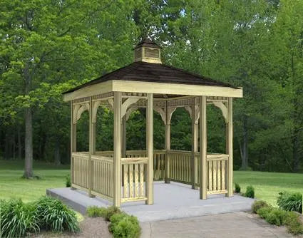 A wooden gazebo with a peaked roof and decorative latticework. The gazebo stands on a concrete base surrounded by greenery.