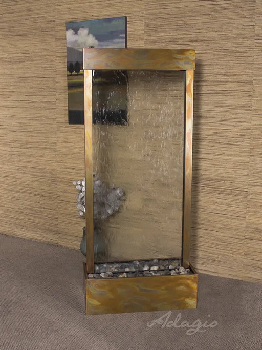 A free standing water fountain, a beautiful adagio water feature. The "Harmony River," features a wide, textured glass panel where water gently cascades down into a shallow basin filled with smooth, grey river stones. 