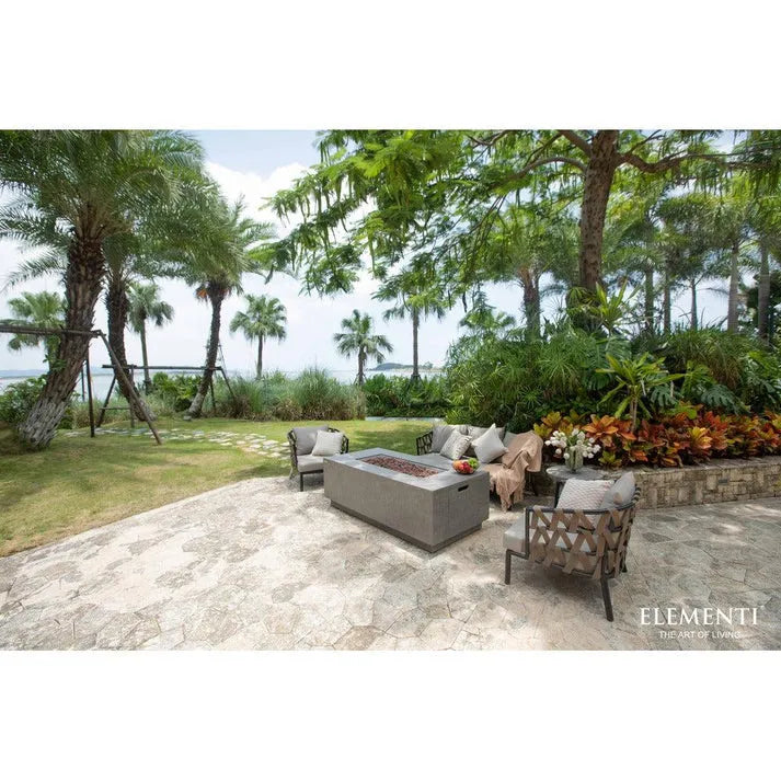 Landscaped backyard patio featuring a contemporary fire table with armchairs and a sofa, overlooking a lake.