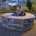 A fire pit made of stone with a fire burning inside. The fire pit is surrounded by a circular stone wall on a patio.