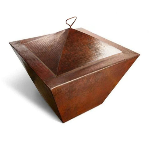 A pyramid-shaped fire pit lid on top of a square fire bowl made of hammered copper with a warm patina. The fire pit has a wide opening at the top and rests on a square base.