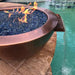 A copper fire pit with a water fountain attachment. The fire pit has a round, hammered copper base and a black steel fire ring.  A water stream jets out from the center of the fire pit.