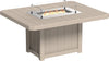 Square outdoor dining table made of weather-resistant tan and brown material with a built-in fire pit and glass wind guard.