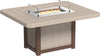 Square outdoor dining table made of weather-resistant tan and brown material with a built-in fire pit and glass wind guard.