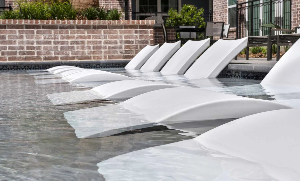 A photo of several white floating lounge chairs arranged in a row in a swimming pool. The chairs have a curved design and appear to be made of a lightweight material.