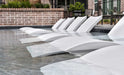 A photo of several white floating lounge chairs arranged in a row in a swimming pool. The chairs have a curved design and appear to be made of a lightweight material.