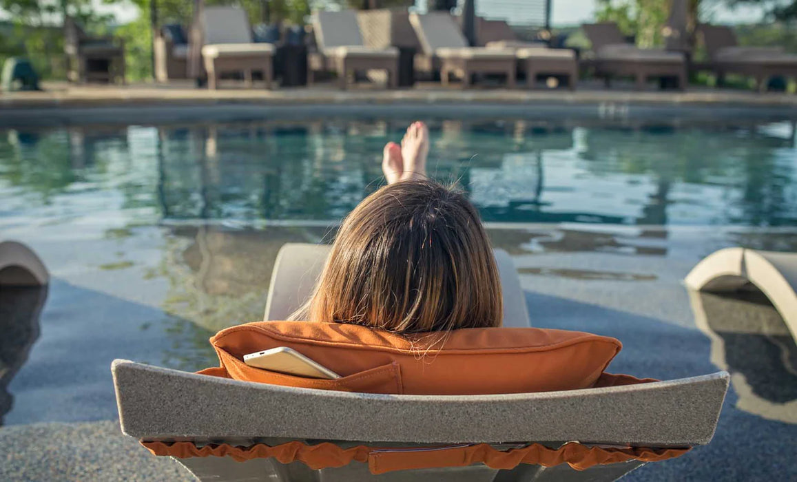 Two white in-pool chaise lounges with blue canopies and patterned pillows, partially submerged in a swimming pool with a light stone deck.