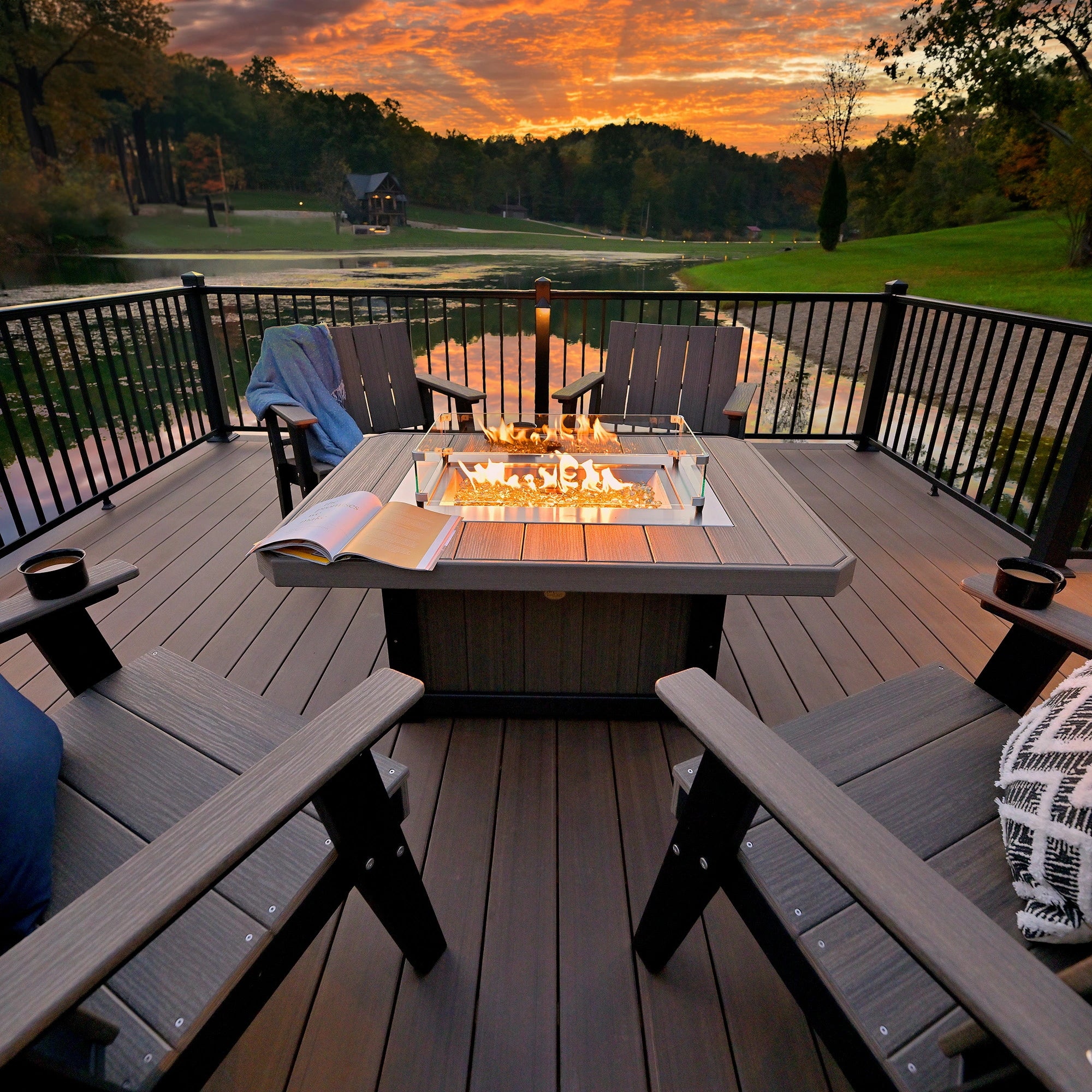 Outdoor fire pit table on a deck with chairs and a scenic sunset view.