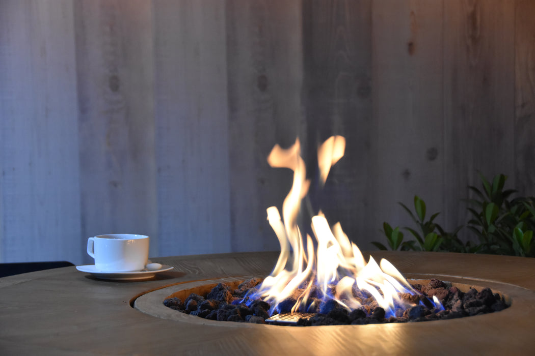 round high top fire pit is lid on brown lava rocks with a cup of coffee on fire table