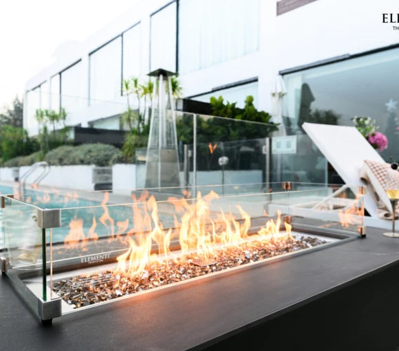 rectangle fire pit table with glass guard in outdoor setting beside the pool