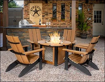 A round fire pit table surrounded by four Adirondack chairs on a patio. The fire pit is burning with flames, and there are wine glasses and a bottle on the table. The chairs are made of the same material as the table, with a slatted design and curved armrests. The background shows a brick wall and a bar area.