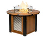 A round, gas-powered fire pit table with a glass flame guard. The table has a woven metal panel on the bottom half and a light brown top. The flames are visible through the glass guard.