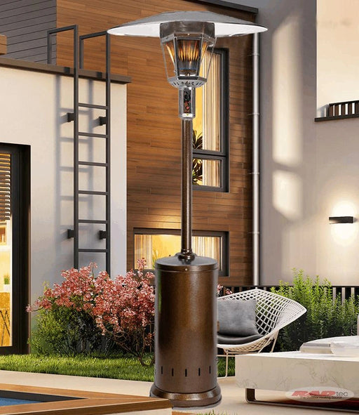 A tall, bronze-colored patio heater with a glass shade and a visible flame, standing on a patio with outdoor furniture.