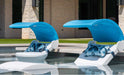 Two white in-pool loungers, each with a retractable blue canopy and blue patterned pillows, partially submerged in a pool with a light-colored stone surround.