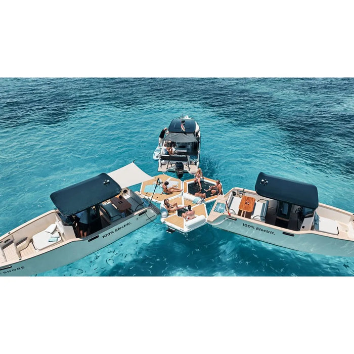 Two electric boats on a body of water attached to a floating platform with people enjoying the outdoors.