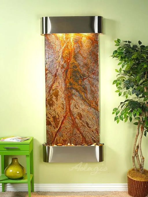 Wall-mounted water feature with decorative stone design on a light green wall, next to a green side table and potted plant.