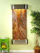 Wall-mounted water feature with decorative stone design on a light green wall, next to a green side table and potted plant.
