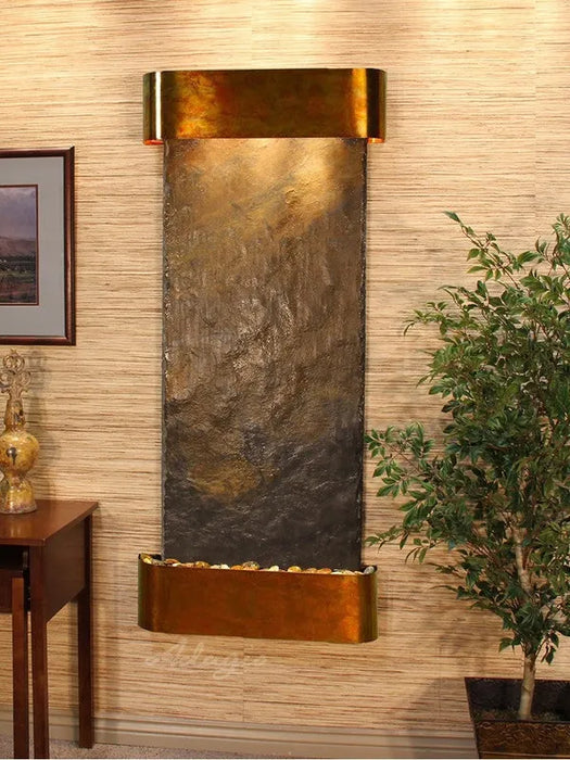 Wall-mounted water feature with bronze finish in a room with a plant and side table.