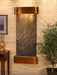 Wall-mounted water feature with bronze finish in a room with a plant and side table.