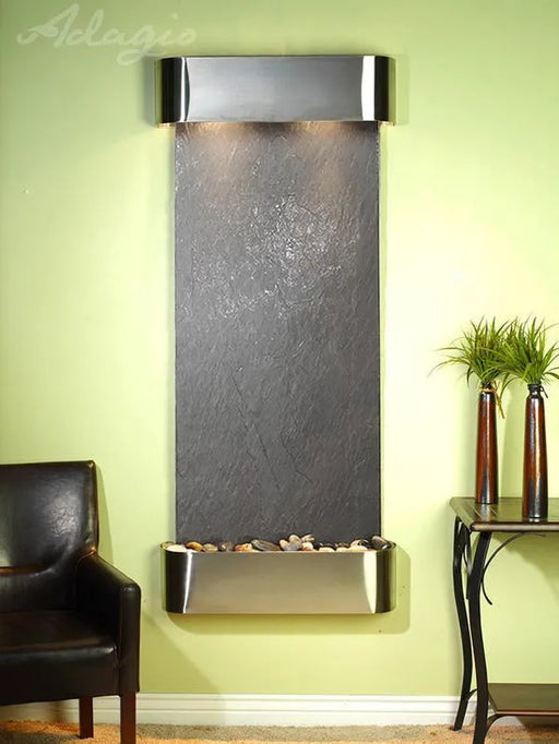 Wall-mounted water feature with dark stone finish and metallic frame against a light green wall.